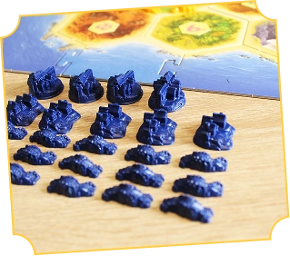 Niebieskie plastikowe figurki osad i dróg są starannie ułożone na stole przed planszą do gry „Katán”