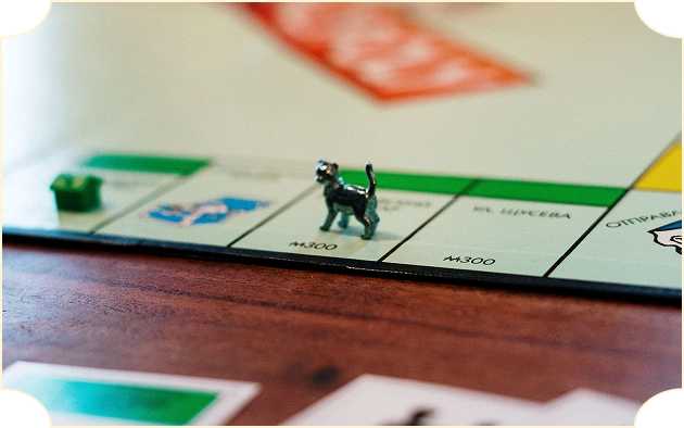 Metalowa figurka kota stoi na zielonej kratce planszy do gry „Monopoly”